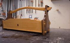 a wooden bed frame sitting on top of a floor next to a wall with tools hanging from it