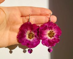 a person holding two pink flowers in their hand with drops of water on the petals