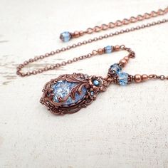 To make this Victorian style necklace, I wrapped an aqua blue glass faux opal cabochon in exquisitely detailed antiqued copper filigree. The stone is set in an antique Victorian style setting and adorned with floral elements and coordinating crystals.---------------------------------------------------------------------------------------------Dimensions and details- Focal cabochon measures 18x13mm- The drop of the entire pendant (top of setting to bottom of setting) is approximately 1 and 3/8 inc Elegant Gemstone Copper Jewelry, Elegant Blue Copper Jewelry, Elegant Copper Filigree Jewelry, Elegant Bronze Wire Wrapped Necklaces, Elegant Antique Finish Adjustable Necklace, Elegant Oval Copper Necklace, Bronze Metal Jewelry With Cabochon Details, Ornate Copper Jewelry With Antique Finish, Elegant Bronze Wire Wrapped Jewelry