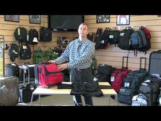 a man standing in front of a table with luggage on top of it and bags hanging from the wall behind him