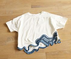 a white t - shirt with blue waves on it sitting on the floor next to a pair of scissors