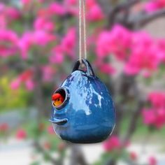 a blue bird feeder hanging from a tree with pink flowers in the backround