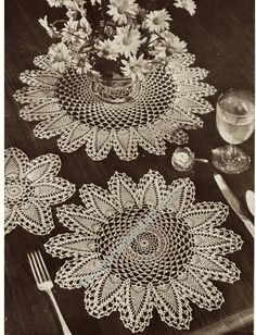 three crocheted doily on a table with flowers in a vase and silverware