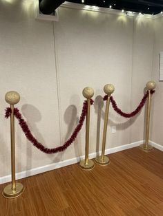 three gold poles with red garland on them in front of a white wall and wooden floor