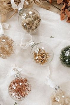 four glass ornaments with dried flowers in them on a white table cloth next to branches