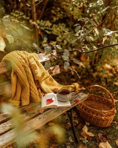 an open book and cup of coffee sit on a wooden bench in the fall leaves