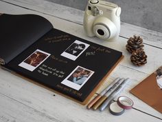 an open book with pictures and pens on it next to a polaroid camera, pine cones, and other items