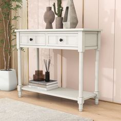 a white console table with two drawers and three vases on top, in front of a pink wall