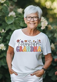 an older woman with glasses standing in front of some flowers and bushes wearing a t - shirt that says grandma