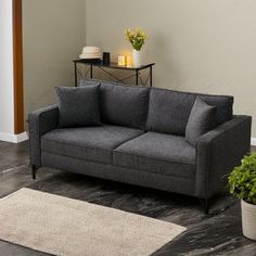 a grey couch sitting on top of a wooden floor next to a potted plant