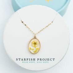 This necklace showcases the beauty of nature, in bloom. Dried yellow flowers are encased in clear resin within a 14K gold plated setting and an adjustable 14k plated gold chain, the In Bloom Necklace is perfect for everyday wear and layering alike. Shop the matching drop earrings Made in China Materials: 14k gold plated stainless steel chain with a yellow flower resin oval pendant necklace; Hypoallergenic; lead and cadmium free with nickel content less than 100 ppm Dimensions: chain is 16-18 inc Delicate Oval Jewelry With Pressed Flowers, Gold Hypoallergenic Flower Pendant Jewelry, Delicate Oval Pressed Flower Jewelry, Hypoallergenic Gold Flower Pendant Jewelry, Delicate Pressed Flowers Jewelry For Everyday, Gold 14k Gold-filled Birth Flower Jewelry, 14k Gold Filled Birth Flower Jewelry, 14k Gold-filled Birth Flower Jewelry, Yellow Gold Jewelry With Pressed Flowers In Round Pendant