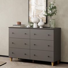 a gray dresser with vases and flowers on it in front of a framed painting