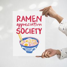 a person holding up a sign with ramen appreciation society written in red on it