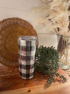 a plaid tumbler sitting on top of a wooden table next to a potted plant