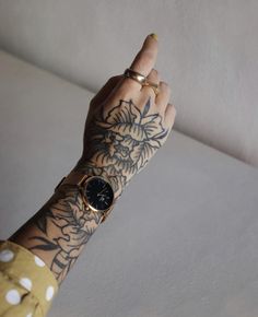 a woman's arm with tattoos and a wrist watch on her left hand, in front of a white wall