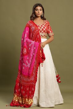 Shop White self-embroidered Zari lehenga set featuring bandhej dual print dupatta and zari & gota patti embroidered red blouse. The lehenga also has a long tassel attached to tie the knot. Pair it with beautiful jewelry to enhance your look. Shop online from Pure Elegance. Red And White Lehenga, White Silk Lehenga, Zari Lehenga, Gota Patti Lehenga, Bandhej Print, Haldi Outfit, White Lehenga, Lehenga Blouse Designs, Lehenga Blouse