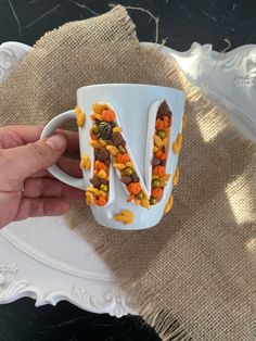 a hand holding a coffee cup with cereal in it and the letter n on top