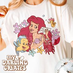 a woman wearing a white shirt with an image of the little mermaid and flounds on it