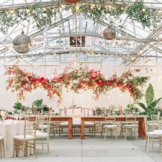 an indoor wedding venue with flowers and greenery hanging from the ceiling, along with long wooden tables