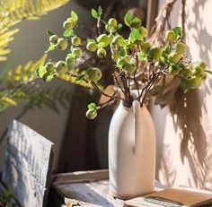 a white vase filled with green plants on top of a wooden table next to a planter