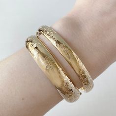 An adult-size polished 14K yellow gold-filled signet bangle bracelet featuring a diagonal space for personalization flanked by floral engraving. The outer shell is solid gold pressure-bonded to an inner core of high-quality brass. Guard and hinge Width: 8 mm Circumference: 7"