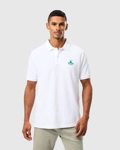 A man stands against a plain background, wearing the Psycho Bunny MENS COURTSIDE PIQUE POLO - B6K655C200. This tennis-inspired white embroidered pique polo features a small green logo on the left chest and is crafted from soft Pima cotton. It has a collar and short sleeves, which he pairs with light-colored pants. The man has short, dark hair and maintains a neutral expression. Bunny Logo, Button Outfit, Swimwear Shorts, Linen Shop, Sweaters And Leggings, Linen Women, Sweater Coats, Swimwear Accessories, Scarf Hairstyles