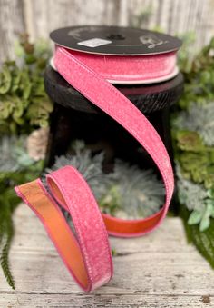 a roll of pink ribbon sitting on top of a wooden table next to green plants