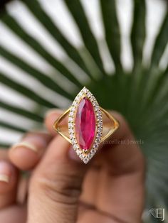 a person holding a ring with a large pink stone in the middle and small white diamonds around it