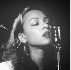 a black and white photo of a woman with her eyes closed while singing into a microphone