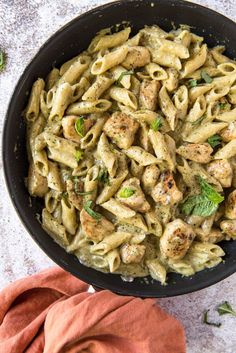 a pan filled with pasta covered in pesto sauce and topped with fresh basil leaves