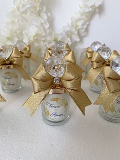 four small glass jars with gold bows and crystal stones in them on a white surface