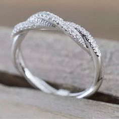 a white gold wedding ring with diamonds on the top and bottom, sitting on a piece of wood