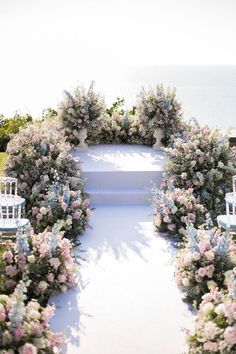 an outdoor wedding ceremony with white chairs and pink flowers on the aisle, overlooking the ocean