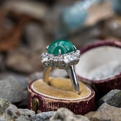 This magnificent ring is centered with one (1) oval cabochon cut natural emerald weighing 5.18 carats and set into a four-prong setting. The emerald is bordered with eight (8), prong set, square step cut diamonds and twelve (12), prong set, round brilliant cut diamonds. The ring measures 23.1mm at the top, rises 12.2mm above the finger, tapering to 3.8mm wide and 1.9mm thick at the base of the shank. This ring is currently a size 7.25. Emerald Cabochon, Step Cut, Cabochon Ring, October Birth Stone, Brilliant Diamond, Natural Emerald, Oval Cabochon, Round Brilliant Cut Diamond, High Quality Jewelry