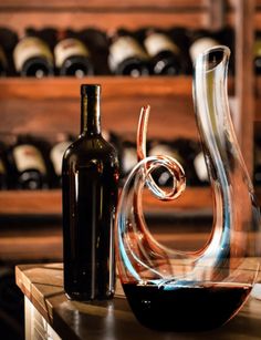 a wine bottle sitting next to a glass vase on top of a wooden table with bottles in the background