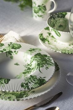 a table set with green and white plates, silverware and utensils on it