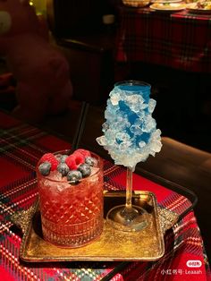 a blue and red drink sitting on top of a table next to a glass filled with berries