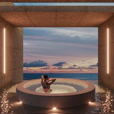 a woman sitting in the middle of a large pool with water around her and lights on either side