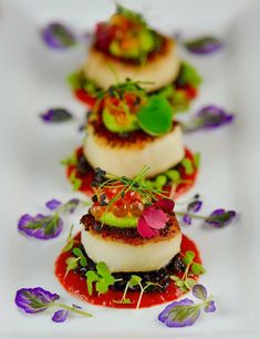 small appetizers are lined up on a white plate with purple and green flowers