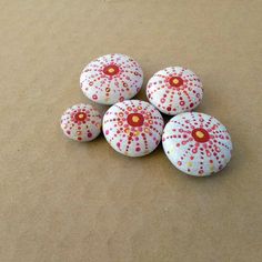 five painted rocks sitting on top of a brown paper covered ground with red and white dots