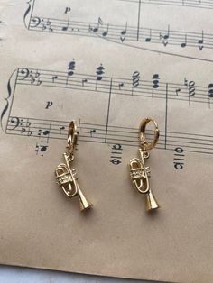 two gold tone trumpet charms sitting on top of sheet music