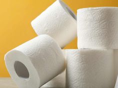 several rolls of toilet paper stacked on top of each other in front of a yellow wall