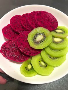 a white plate topped with sliced kiwis on top of green and red fruit