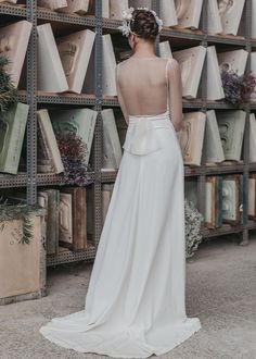 a woman in a white wedding dress standing next to shelves with books and flowers on them