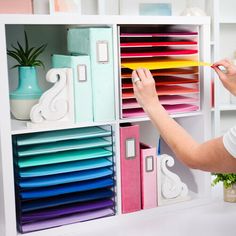 a woman is holding a pencil in her hand and looking at some colorful file boxes