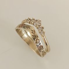 two gold wedding rings with flowers and leaves on each band, set against a plain white background