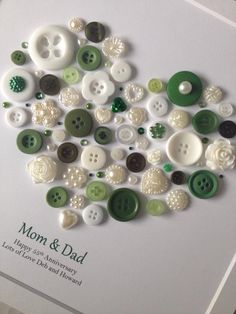 there is a heart made out of buttons on the white surface with words mom and dad written below it