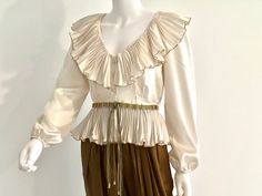 STUNNING vintage C1970s high end, off white or ivory sumptuous long sleeve silk blouse by Partique, featuring a lavish V neck collar with pleated ruffles fully edged in gold trim, a peplum hem, also with pleated ruffles fully edged in gold trim, and a three button front closure.  Channeling Old Hollywood elegance and glamour, this rare beauty is a guaranteed head turner! Approximate Measurements:      Chest: 38"; Shoulder: 16"; Waist: 27"; Length: 19 1/2"      Labeled a Size 6 Please Note:  Part Vintage Beige Blouse For Party, Vintage Beige Party Blouse, Vintage Cream Party Blouse, Poet Blouse, V Neck Collar, Party Blouse, Fashion Illustration Dresses, Rare Beauty, Ivory Silk