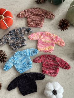 knitted sweaters and mittens laid out on a table next to pine cones