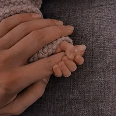 two hands holding a baby's hand on top of a gray couch with a brown blanket